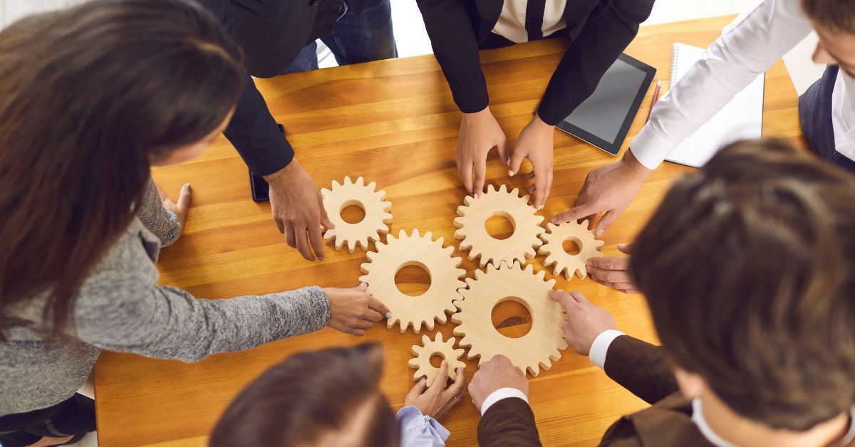 Team assembling wooden gears to represent aligned HR consulting services for compliance and risk management.