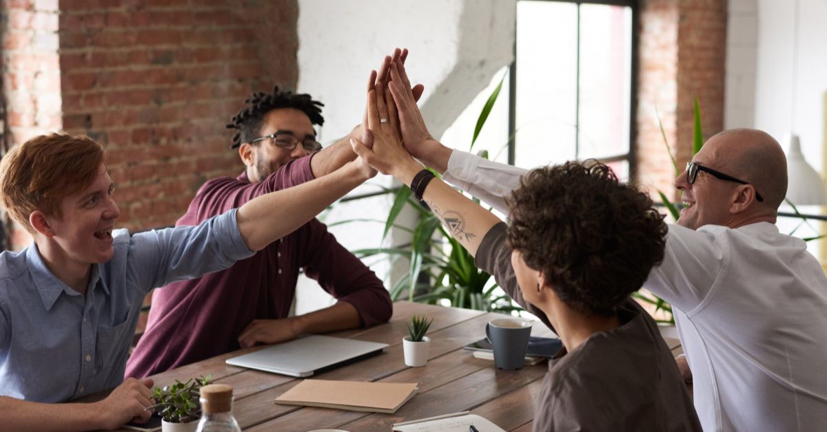 Happy team high-fiving around a meeting table, symbolizing strong culture and employee engagement through HR consulting services.